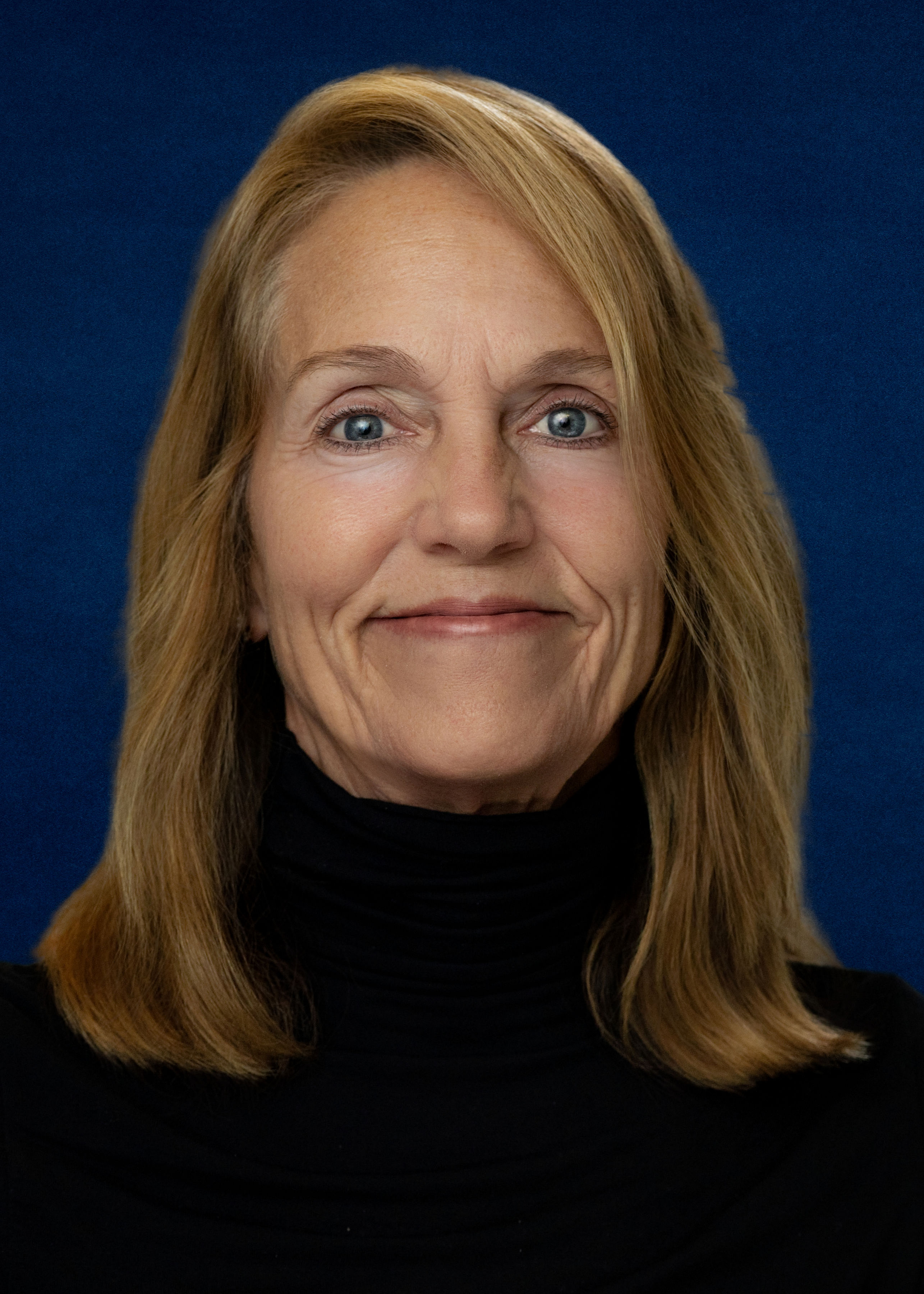 A close-up, photographic portrait concept for Kris Johnson represented symbolically: a smart, neatly tailored navy blazer hung on a simple wooden coat stand, with a small Northfield riverfront scene framed on the wall behind it. The blazer's textured fabric is sharply detailed, with a subtle campaign-colored lapel pin rendered as an abstract shape instead of a logo. Soft side lighting from a nearby window creates gentle highlights and shadows, producing a calm, trustworthy mood. Shot at eye level with shallow depth of field, the focus rests on the blazer and pin while the framed town scene blurs slightly, suggesting professional, community-rooted leadership without showing an actual person.